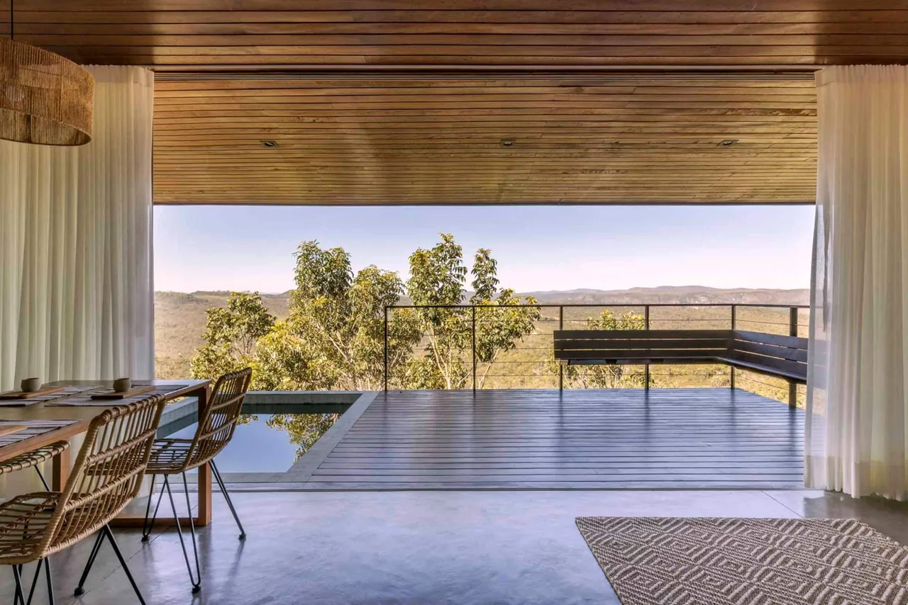 Sala da Casa Jacarandá aberta para o deck, a piscina e a serra