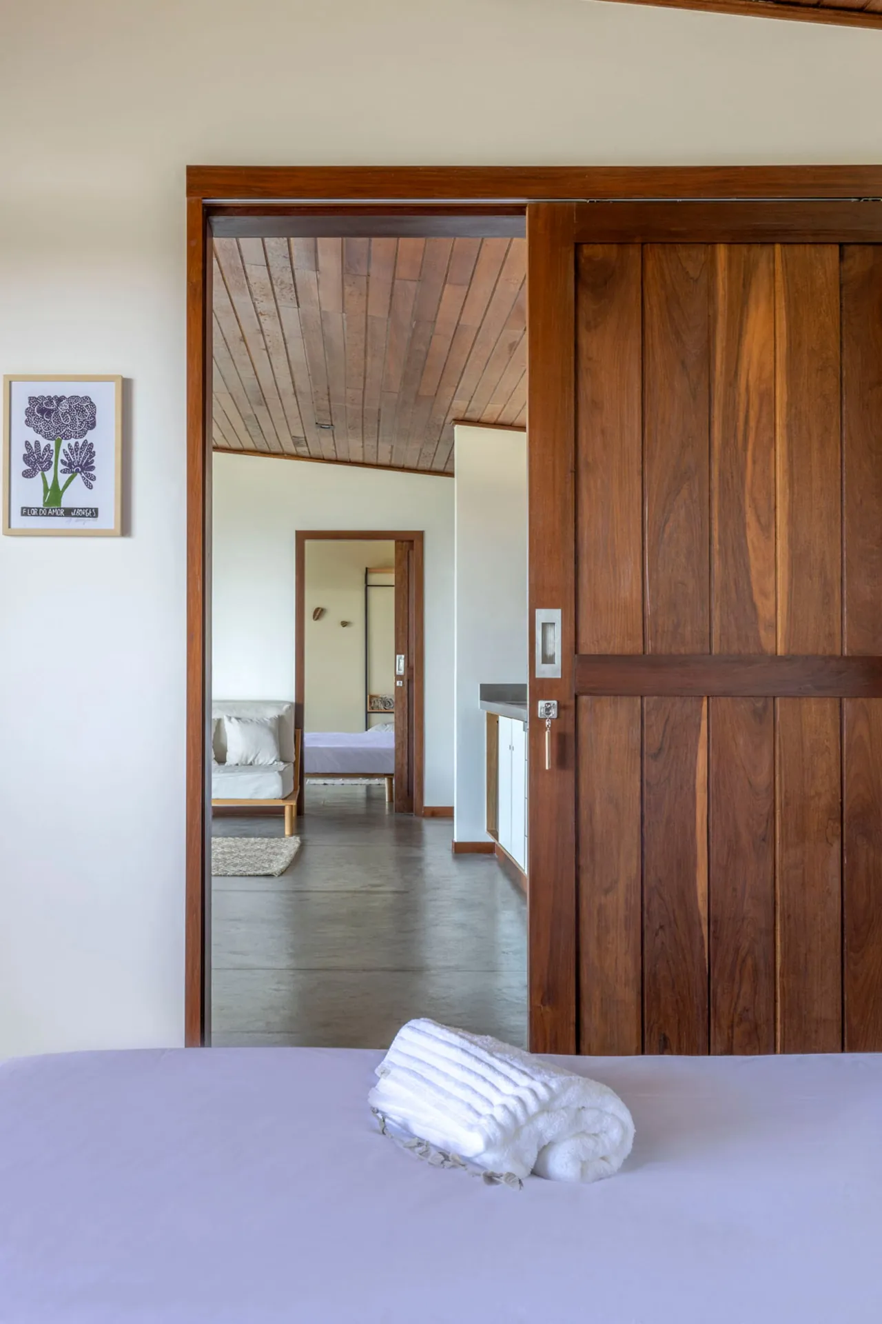 Suíte da Casa Jacarandá com porta de madeira e cama feita